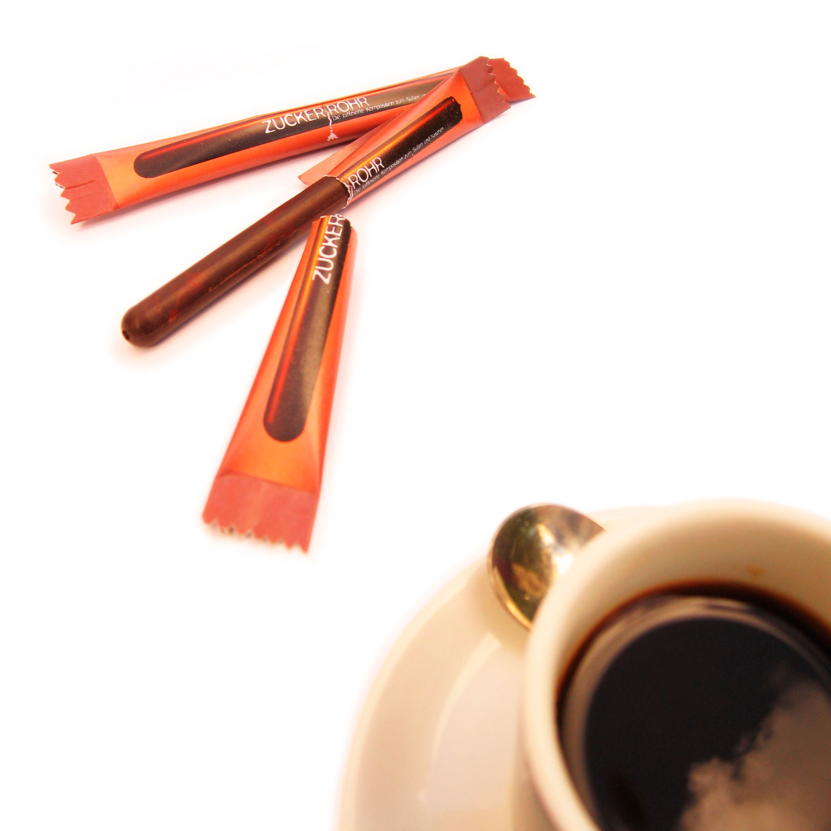 Ein Zuckerröllchen liegt neben einer Tasse Kaffee